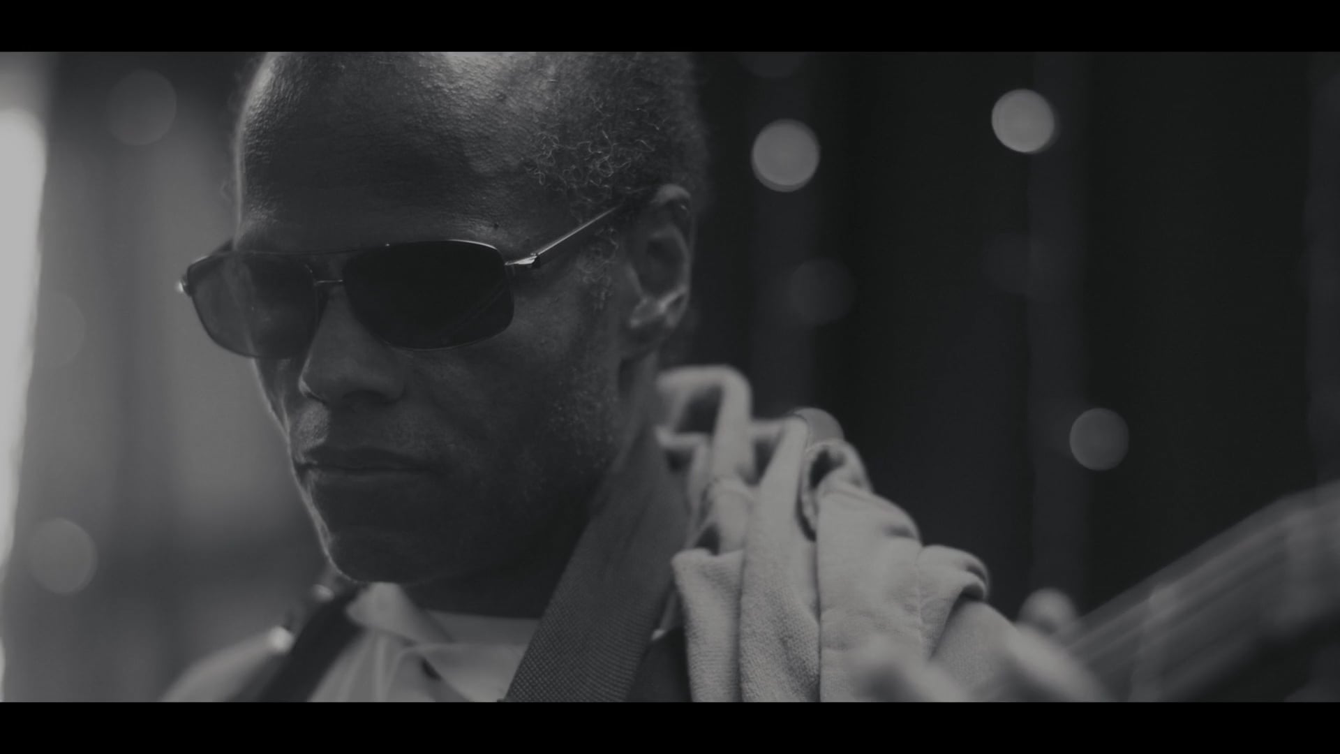 Black-and-white close-up of a musician wearing sunglasses during a live performance.