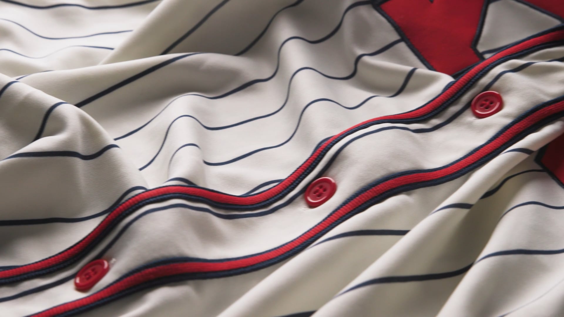 Close-up of a pinstriped baseball jersey with red buttons and trim in a classic vintage style.