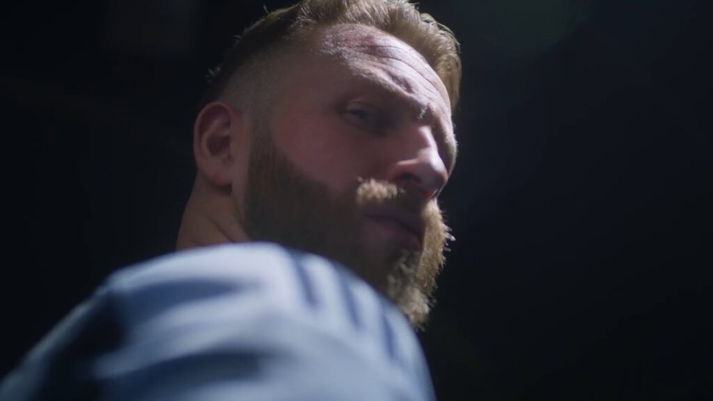 Close-up of a bearded athlete looking over his shoulder under dramatic studio lighting.