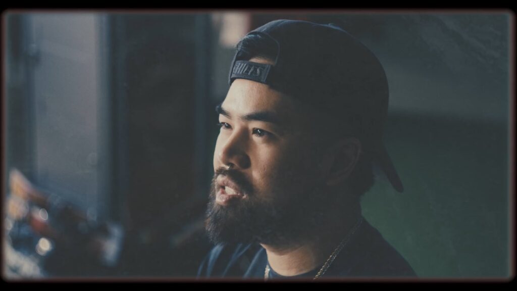 Portrait of a bearded man in a backward cap, looking thoughtfully to the side in soft indoor light.
